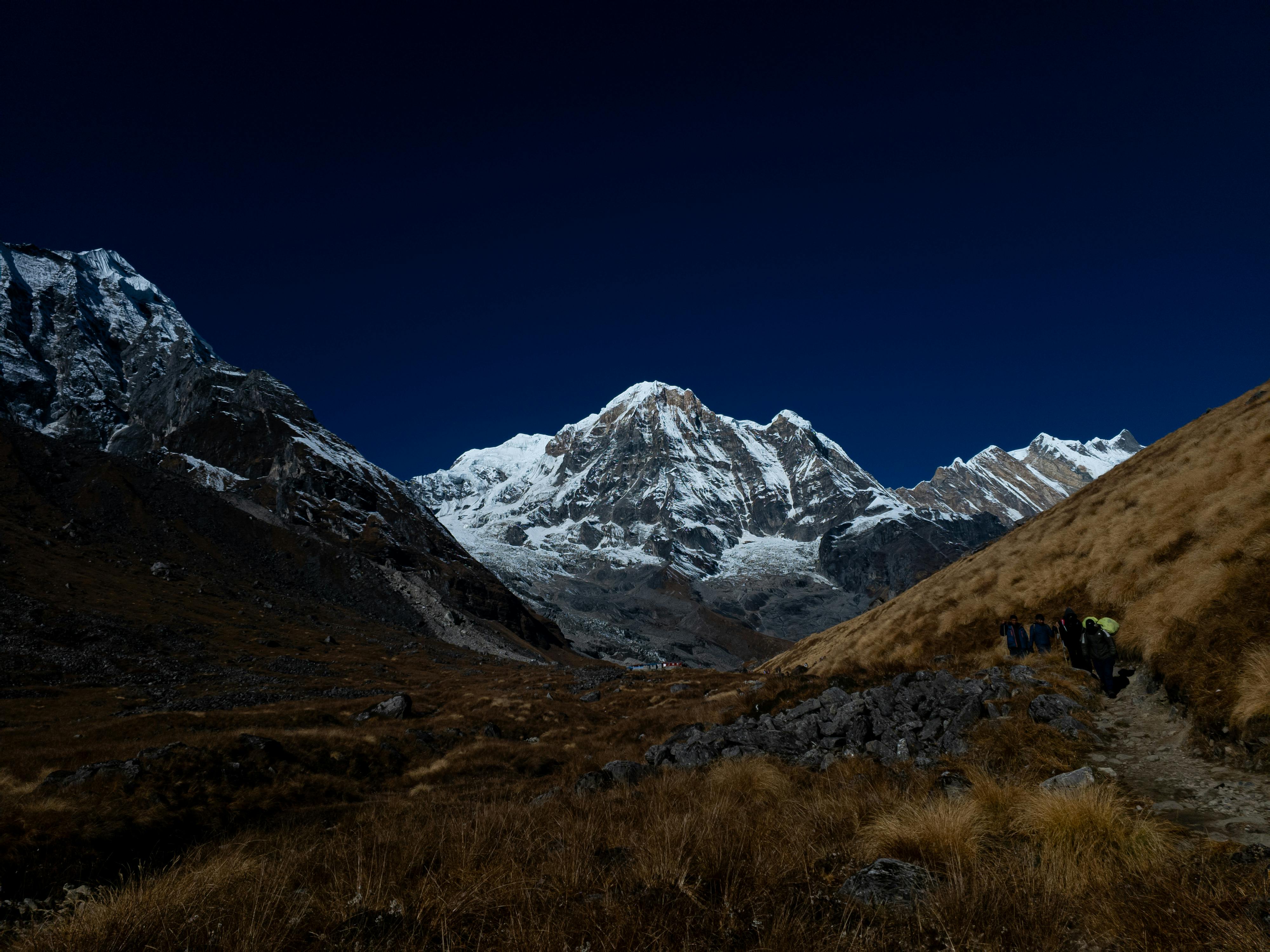 Prescription Goggle Inserts - Trekkers in the Himalayas ascend towards a breathtaking snow-capped peak under a vibrant blue sky.