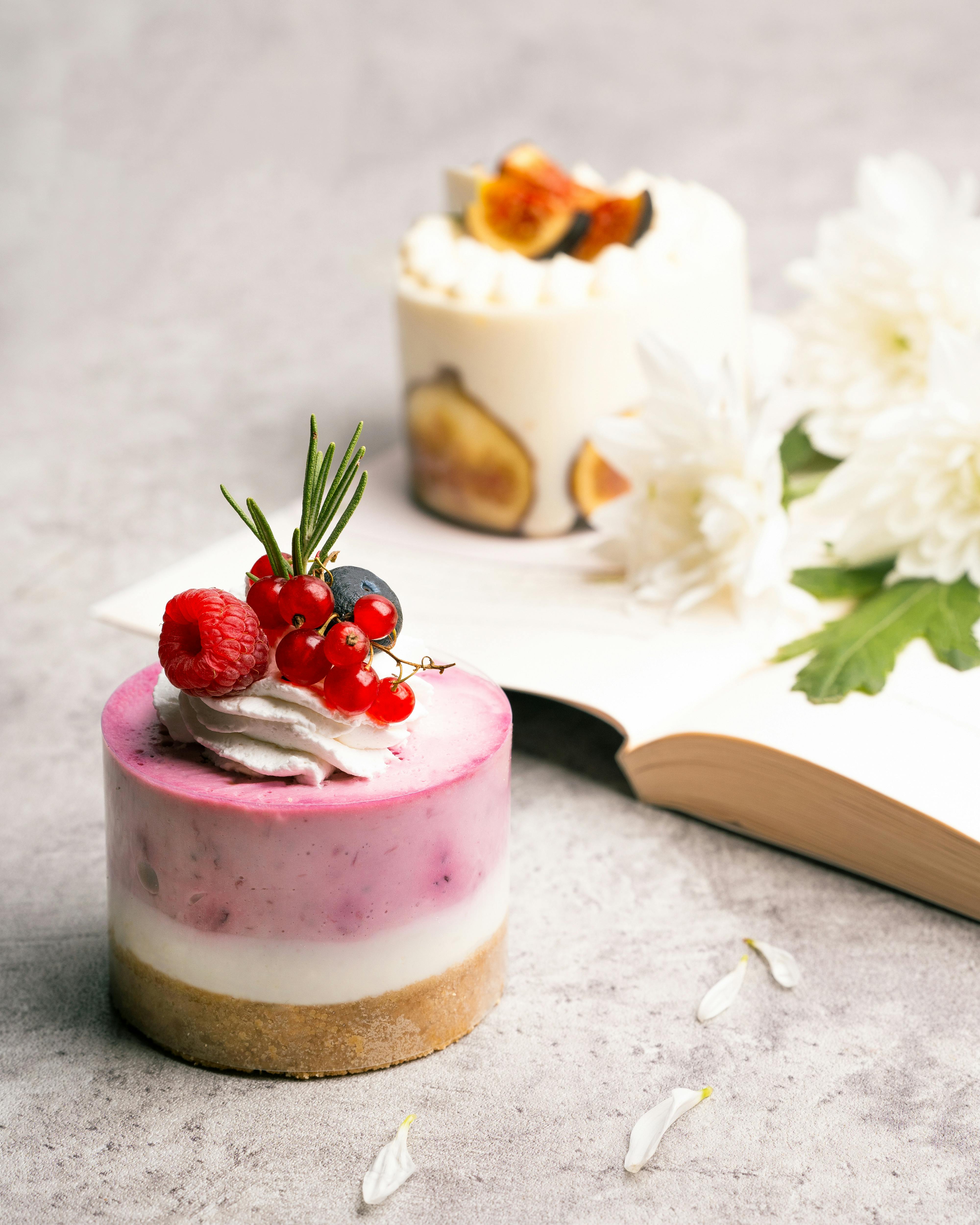 Close-up of stylish berry and fig cheesecakes on marble table with flowers.