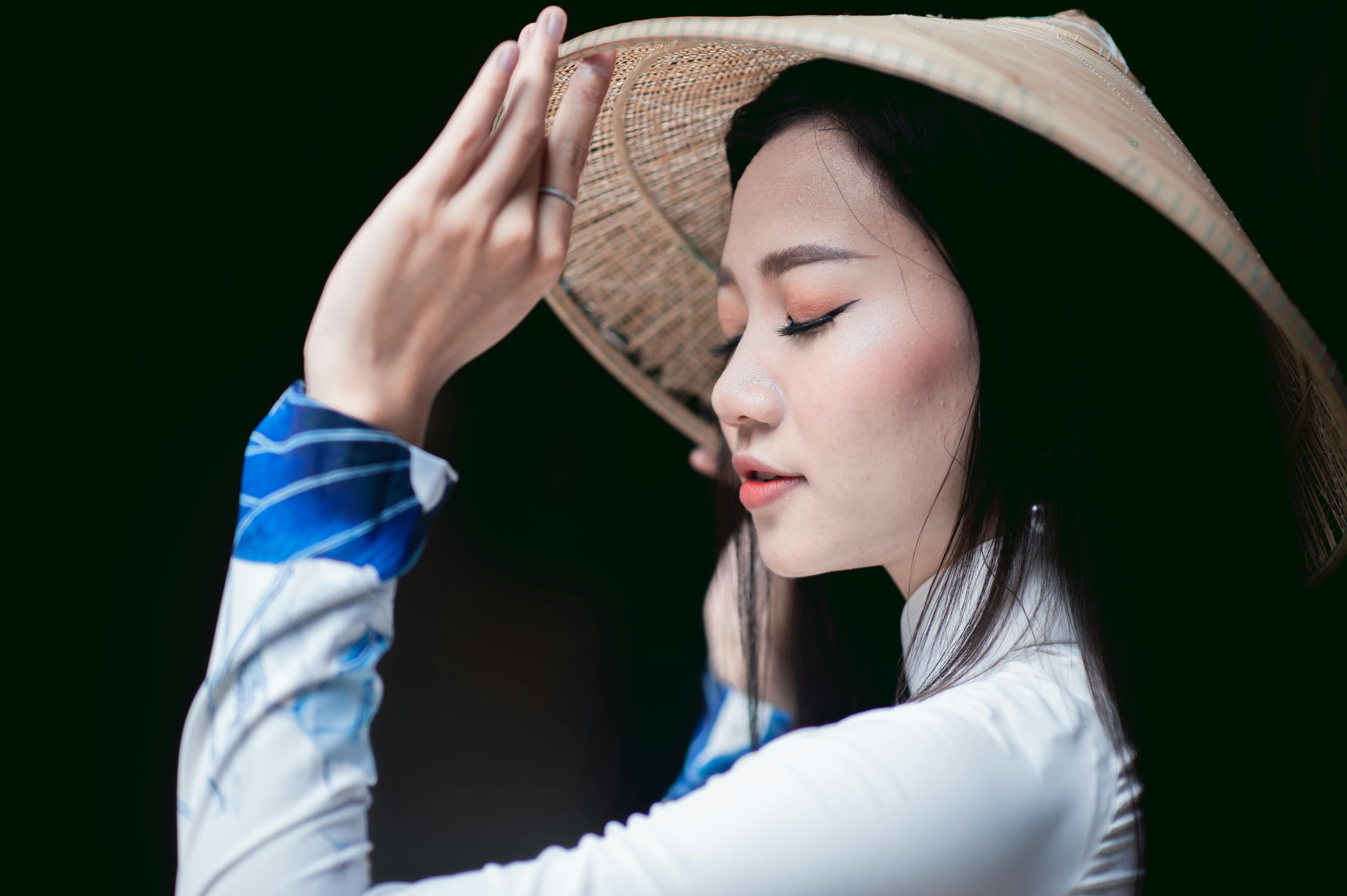 Side profile of a woman in a Vietnamese Ao Dai wearing a conical hat, deep in thought.