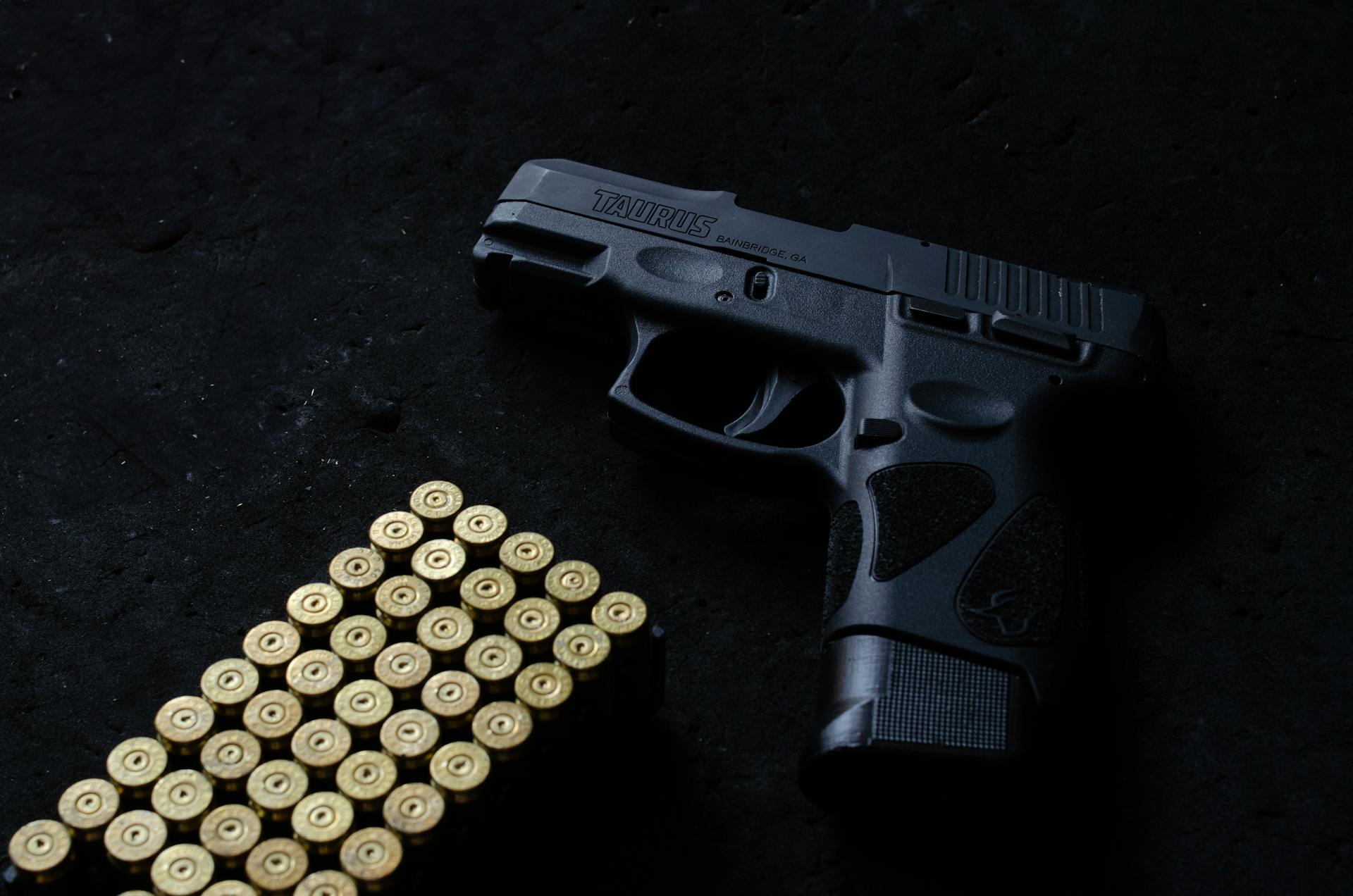 Close-up of a Taurus handgun and bullets on a dark surface, highlighting firearm safety and security themes.