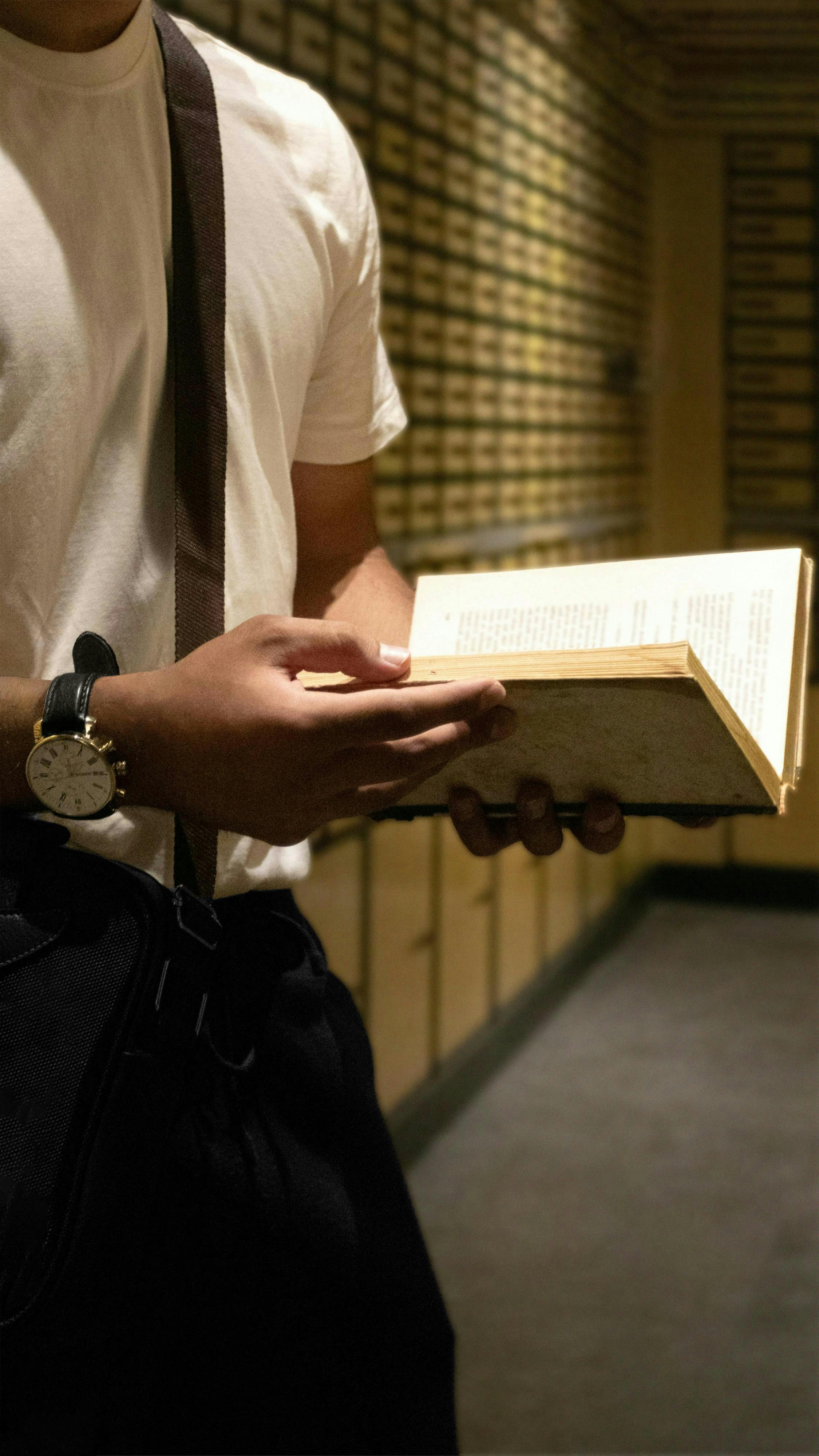 bezplatná Muž stojí v knihovně a drží otevřenou knihu a zaměřuje se na čtení. Základová fotografie