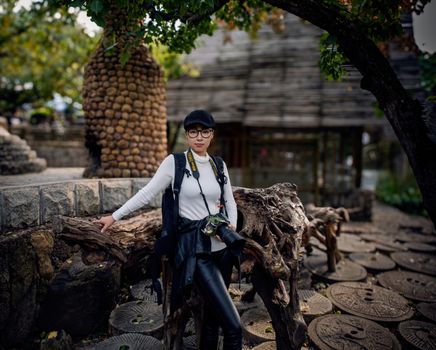 A woman poses confidently outdoors with a camera in a scenic park.