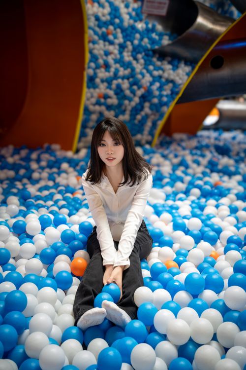 Free Young woman sitting in a colorful ball pit, enjoying leisure time indoors. Stock Photo