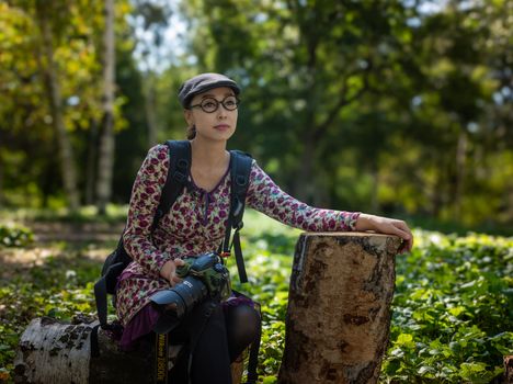A woman photographer in a floral dress with a camera in a lush forest environment.