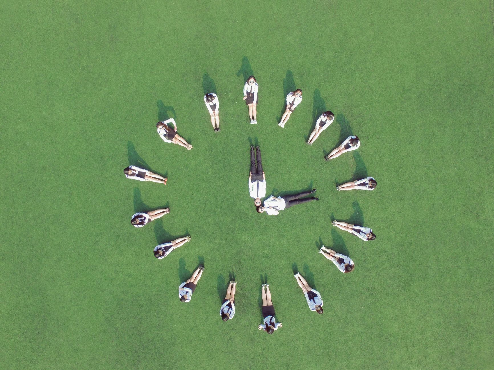 Aerial view of students forming a clock shape on a green field, symbolizing teamwork and time management.