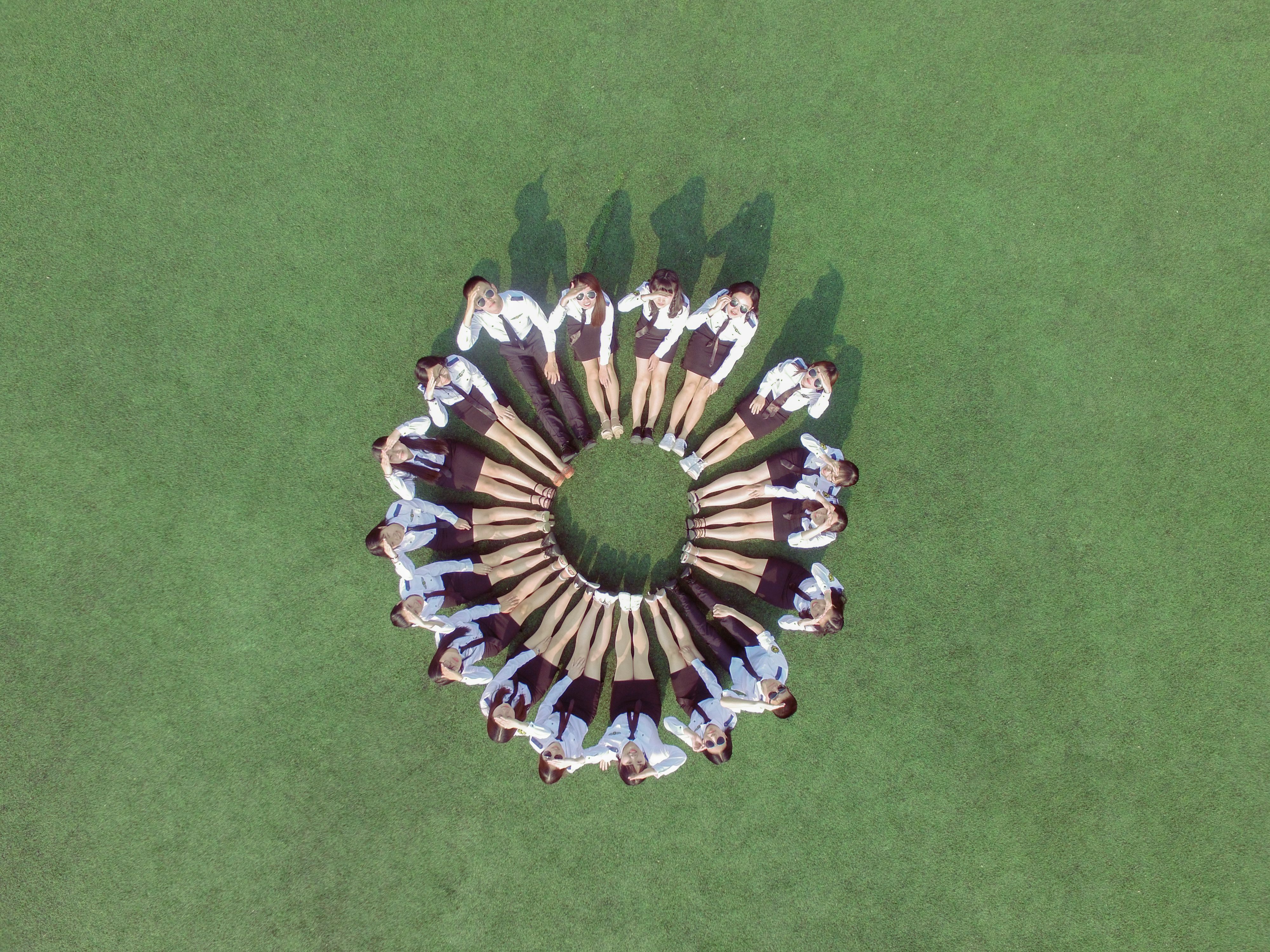 Students forming a circle on grass, aerial shot with creative alignment.