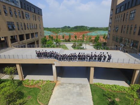 Aerial view of students in graduation gowns on a bridge between buildings.