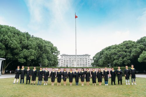 Free Group of university graduates in academic gowns pose outdoors with a flag and building in the background. Stock Photo