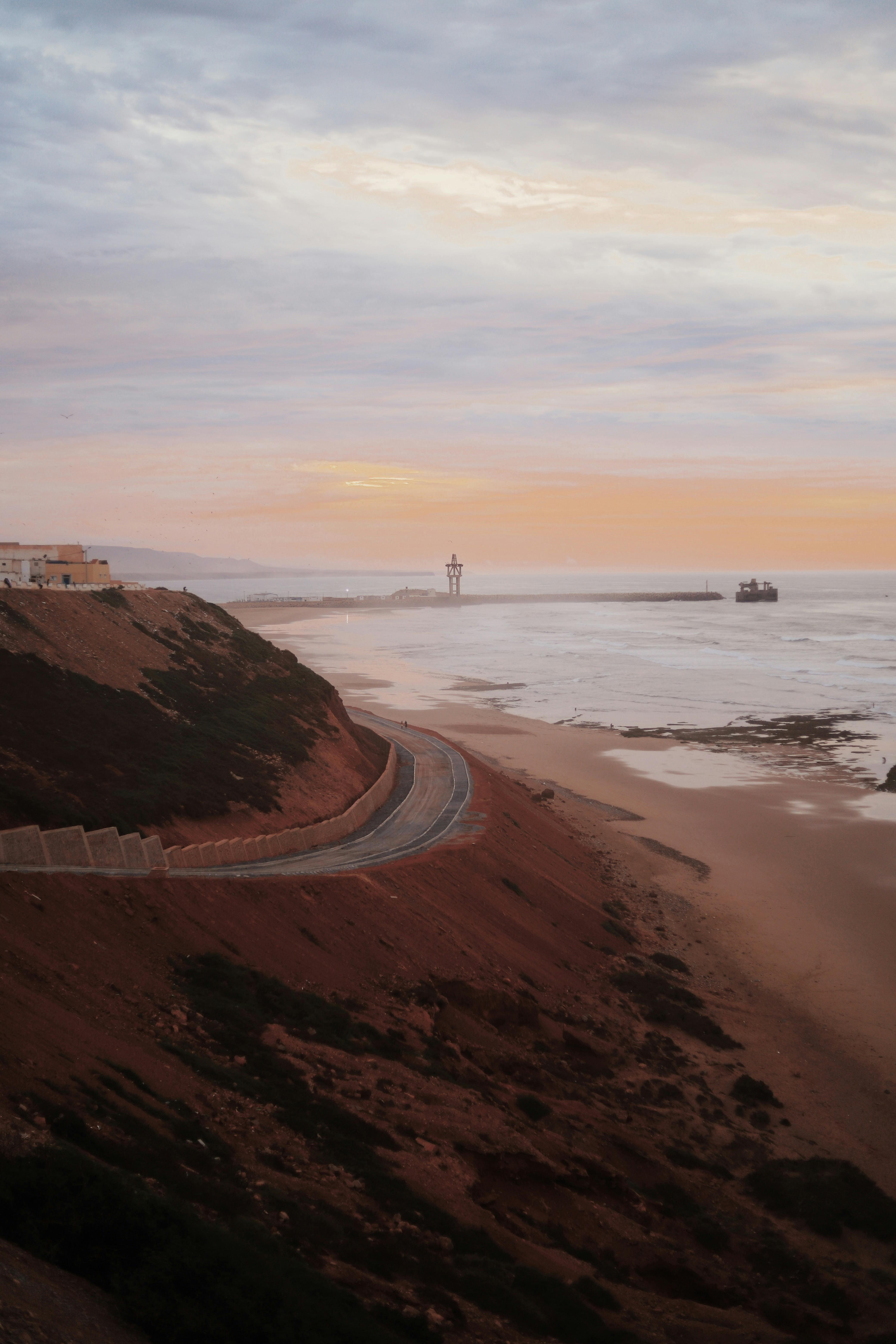 Atmospheric view of a coastal road at sunset with distant ocean horizon and dramatic sky.