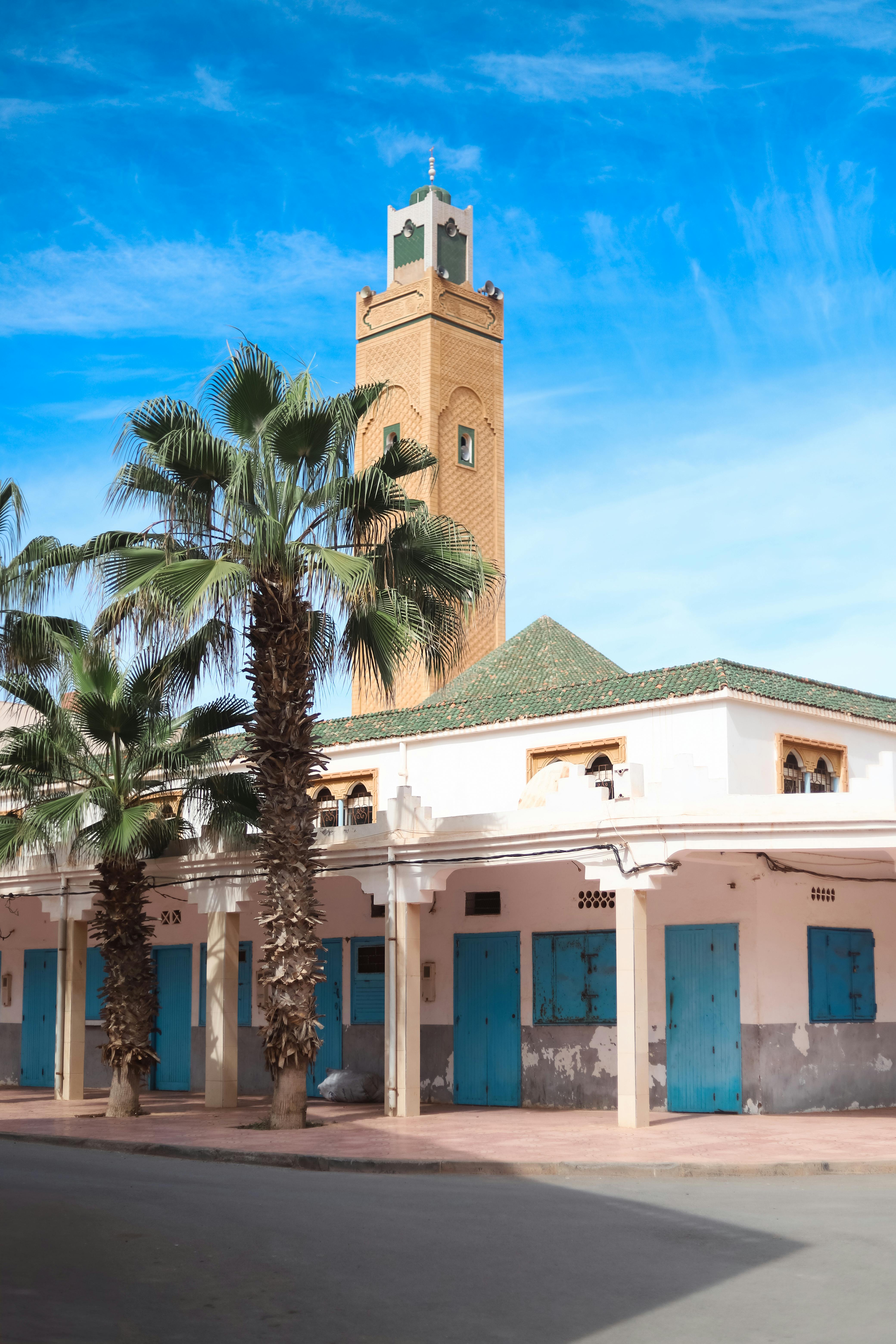 Beautiful Moroccan building with tall minaret and palm trees under a blue sky.