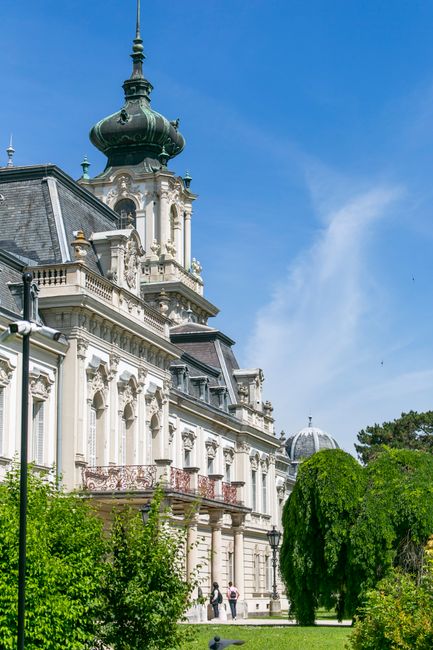 Elegant Baroque palace architecture against a clear blue sky, surrounded by lush greenery in Węgry.