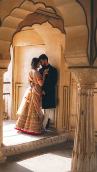 A couple intimately poses in traditional Indian attire amidst historical architecture.