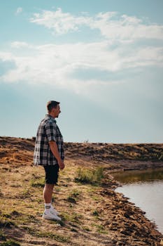 一个年轻人穿着休闲服，站在宁静的湖边，享受着阳光灿烂的日子