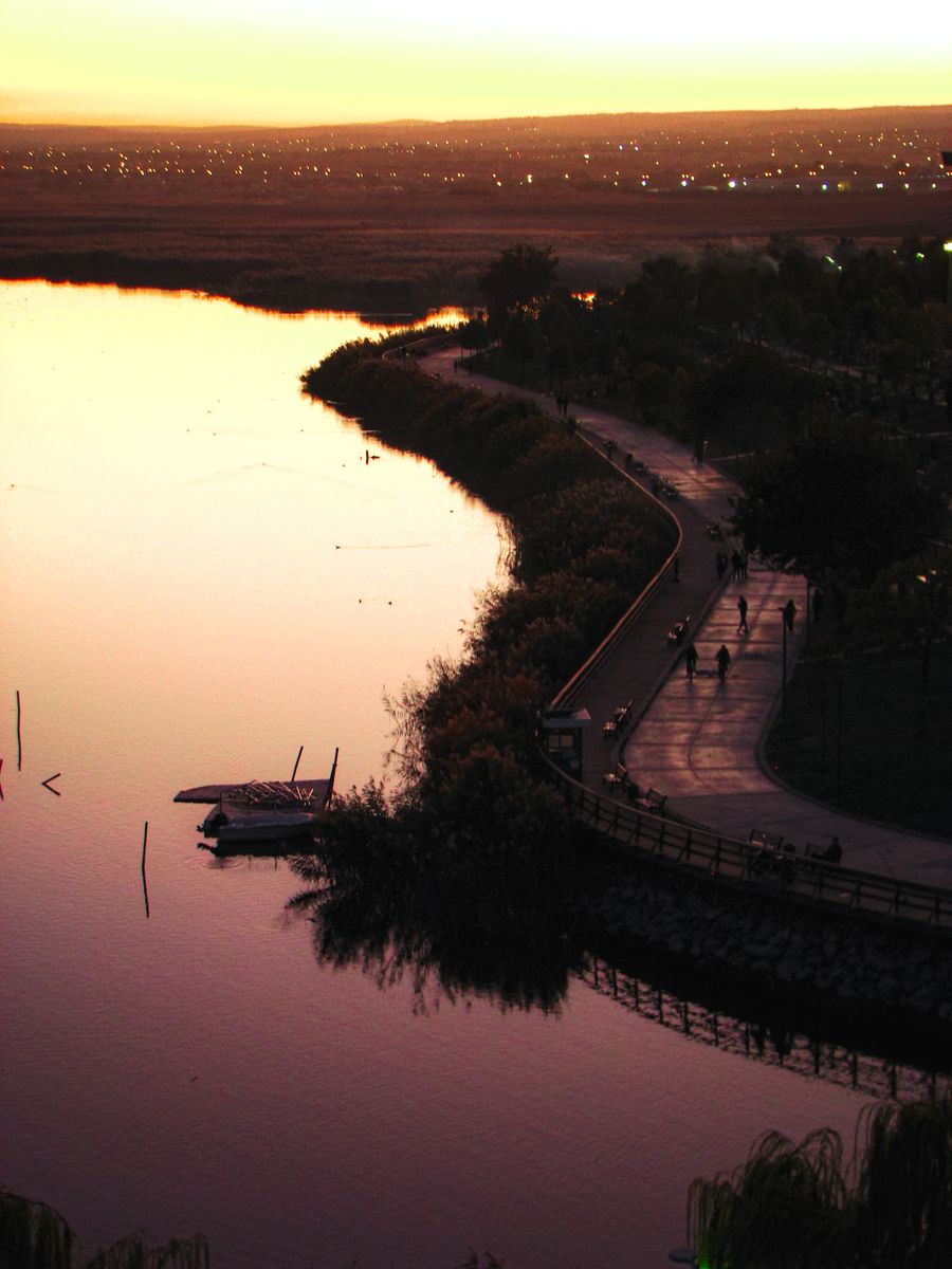 Evening light along a waterfront promenade at dusk, with figures walking the path.