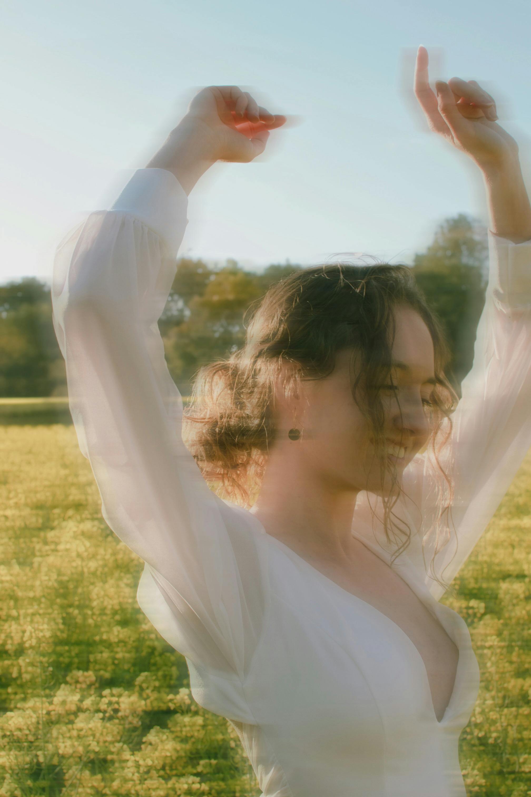 A joyful young woman dancing in a sunny flower field with a warm smile.