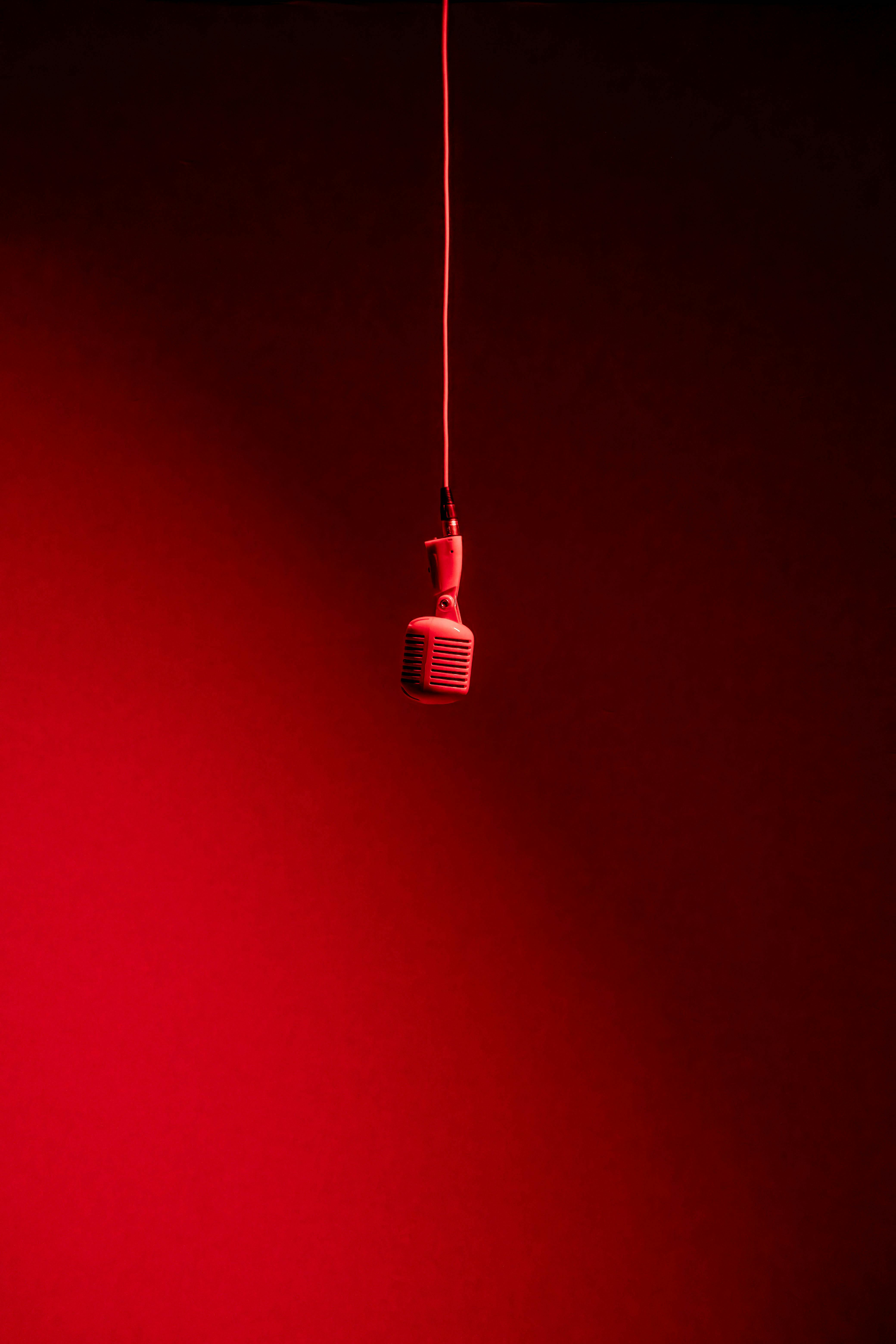 Ücretsiz Minimalist bir düzenlemede kırmızı bir arka plana asılı, çarpıcı kırmızı bir mikrofon. Stok Fotoğraflar
