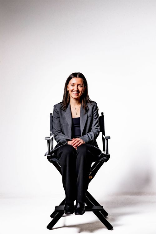 Free Portrait of a smiling woman seated in a director's chair against a white studio backdrop. Stock Photo