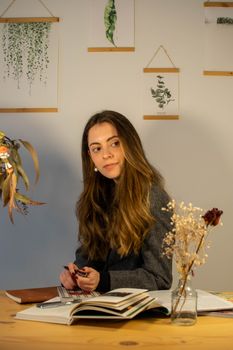 A young woman sits at a desk writing, surrounded by books and plants, creating a cozy work atmosphere. 29233080