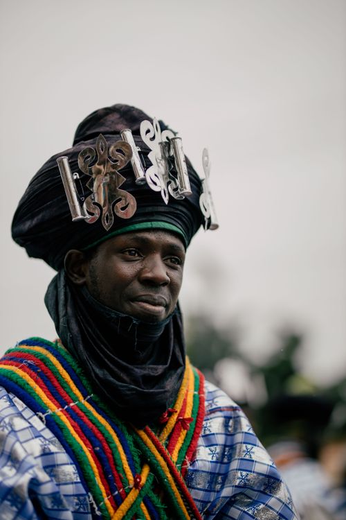Free A man in traditional African costume with colorful layers and ornate headpiece outdoors. Stock Photo