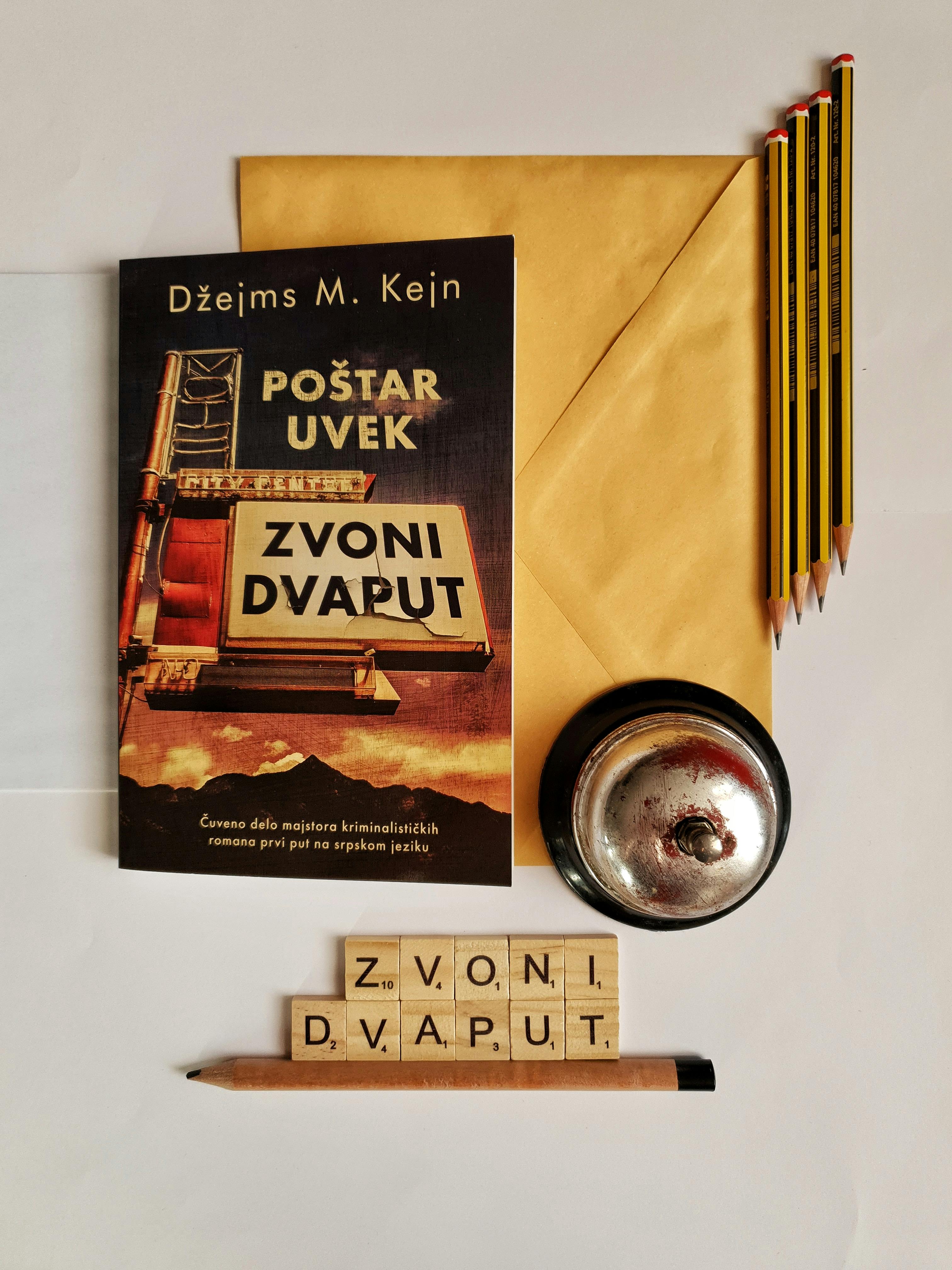Flat lay of a vintage book with pencils, bell, and scrabble tiles on a beige background.