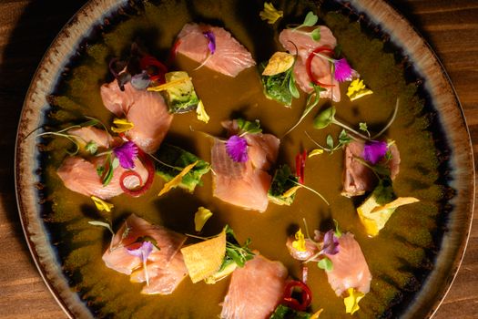 Vibrant salmon crudo dish adorned with edible flowers and herbs on a ceramic plate.