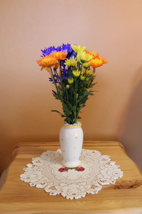 Free Colorful chrysanthemum arrangement in a white vase on lace doily. Perfect for decor themes. Stock Photo