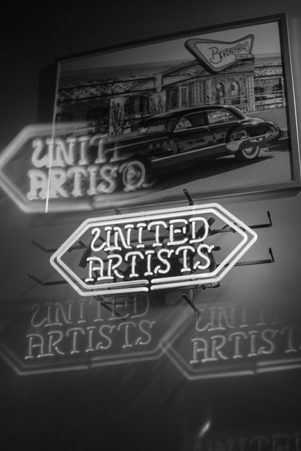 Retro neon sign of United Artists with classic car backdrop and reflections, in black and white.