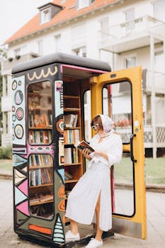 A fashionable woman enjoys a book at a colorful outdoor library booth.