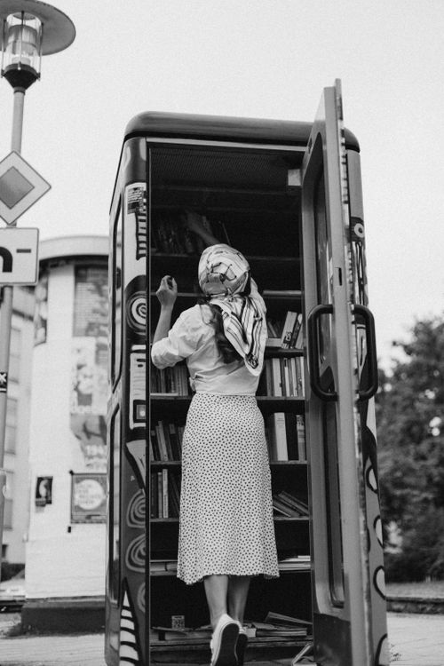 Free Woman in vintage outfit exploring a telephone box library on a city street. Stock Photo