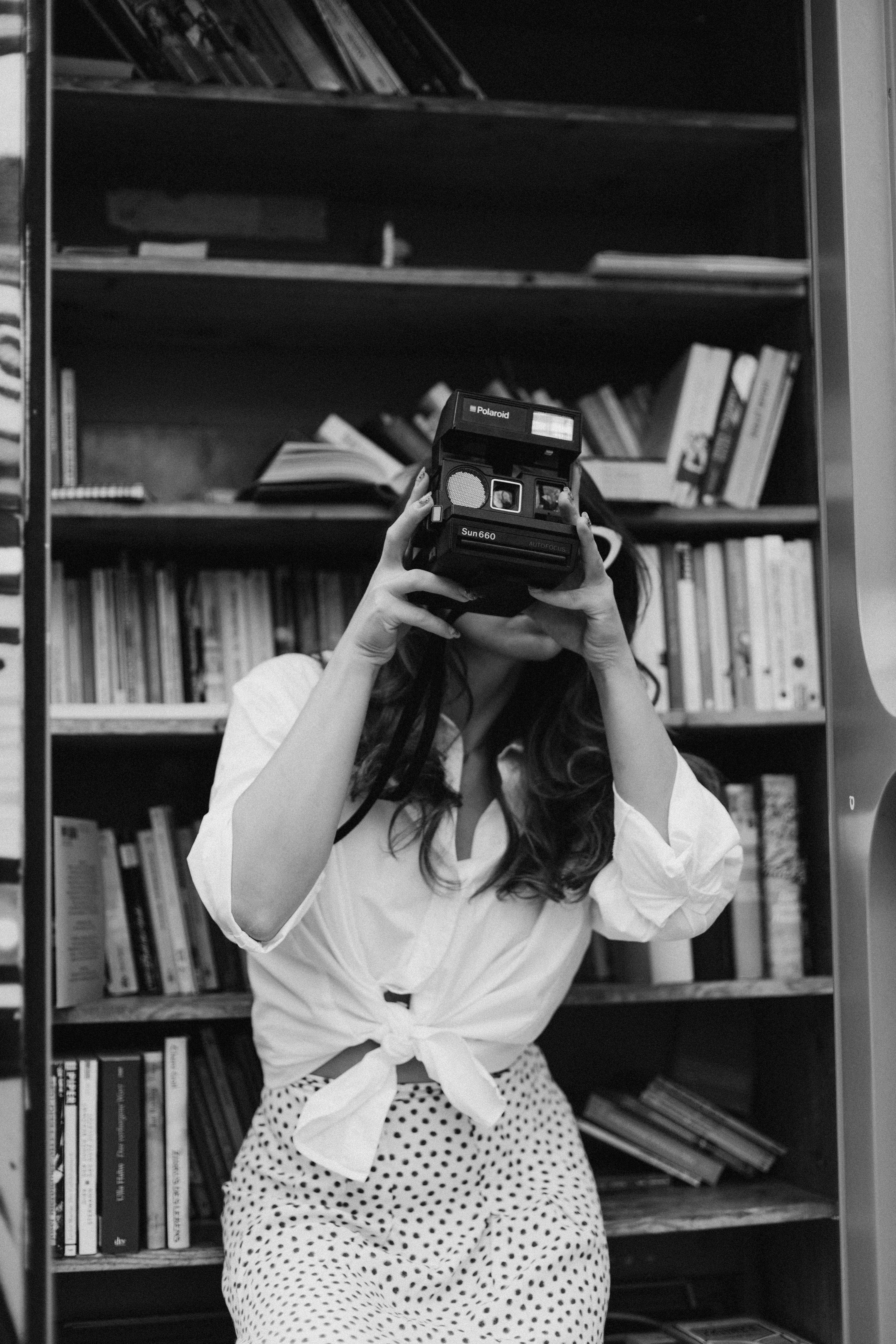 Free Black and white photo of woman using a vintage camera, surrounded by books. Stock Photo
