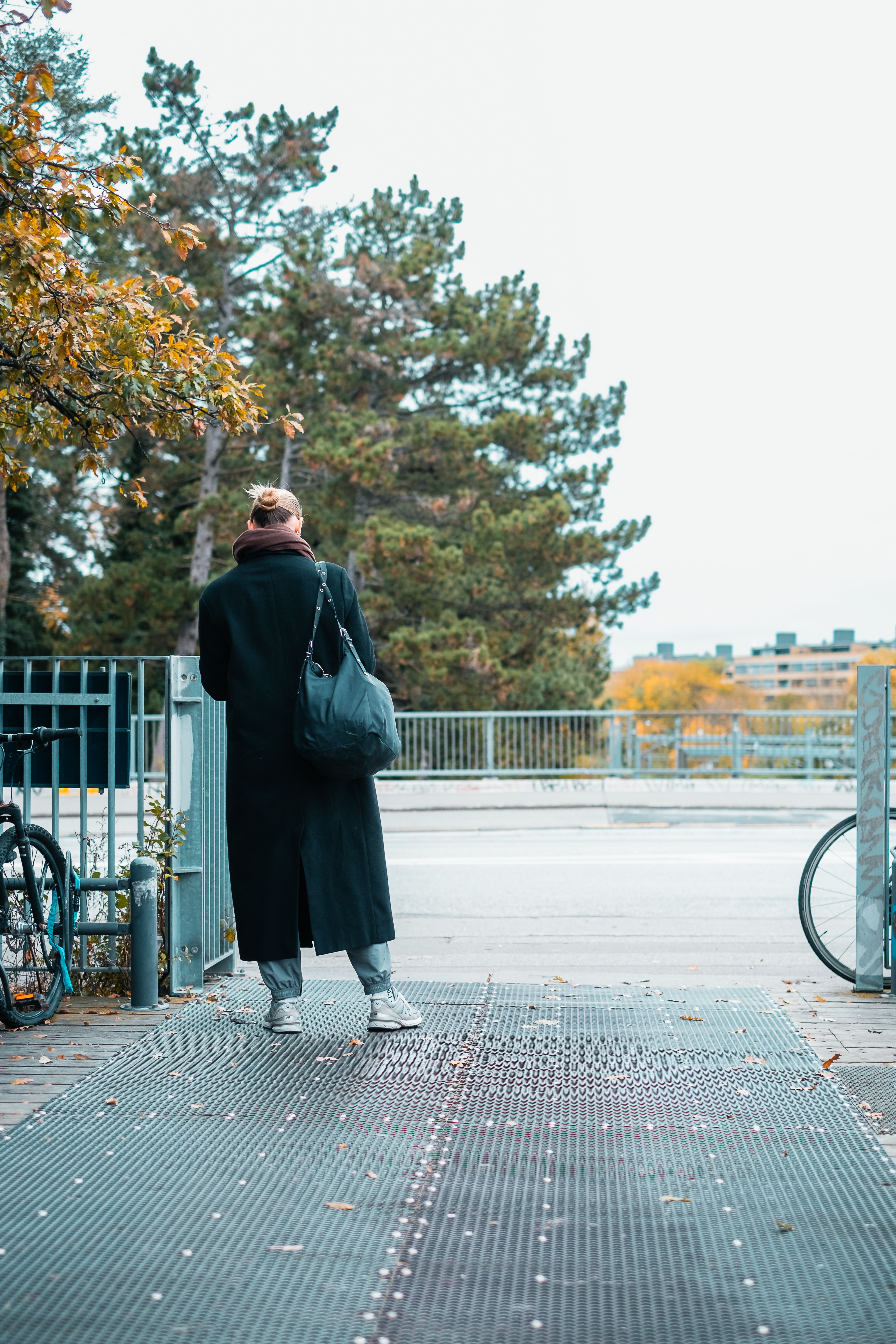 A woman walking on a city bridge surrounded by autumn foliage in Copenhagen, Denmark.