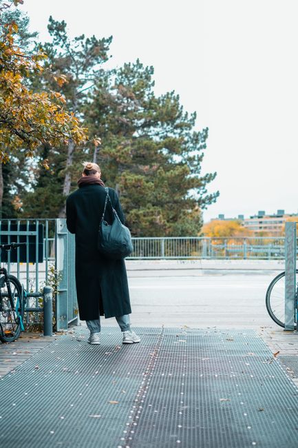 A woman walking on a city bridge surrounded by autumn foliage in Copenhagen, Denmark.