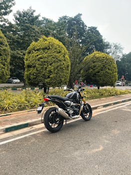A classic black motorcycle parked on a street lined with lush greenery in Bengaluru, India.