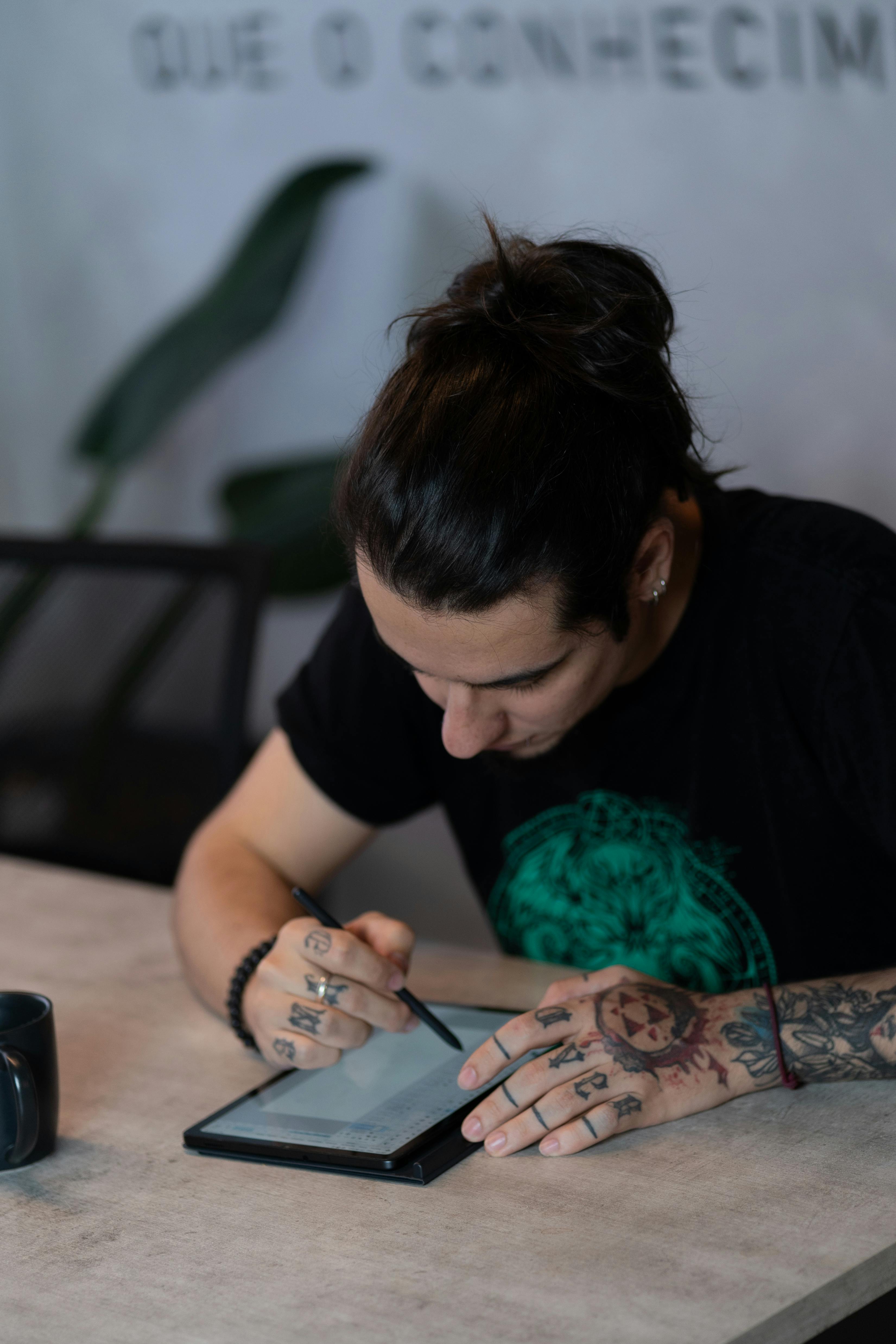 Gratuit Bărbat adult tatuat concentrat pe desenul cu un stilou pe o tabletă digitală într-un cadru modern. Fotografie de stoc