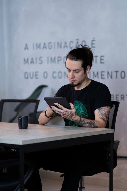 Free Young man with tattoos using a tablet at an office desk. Stock Photo