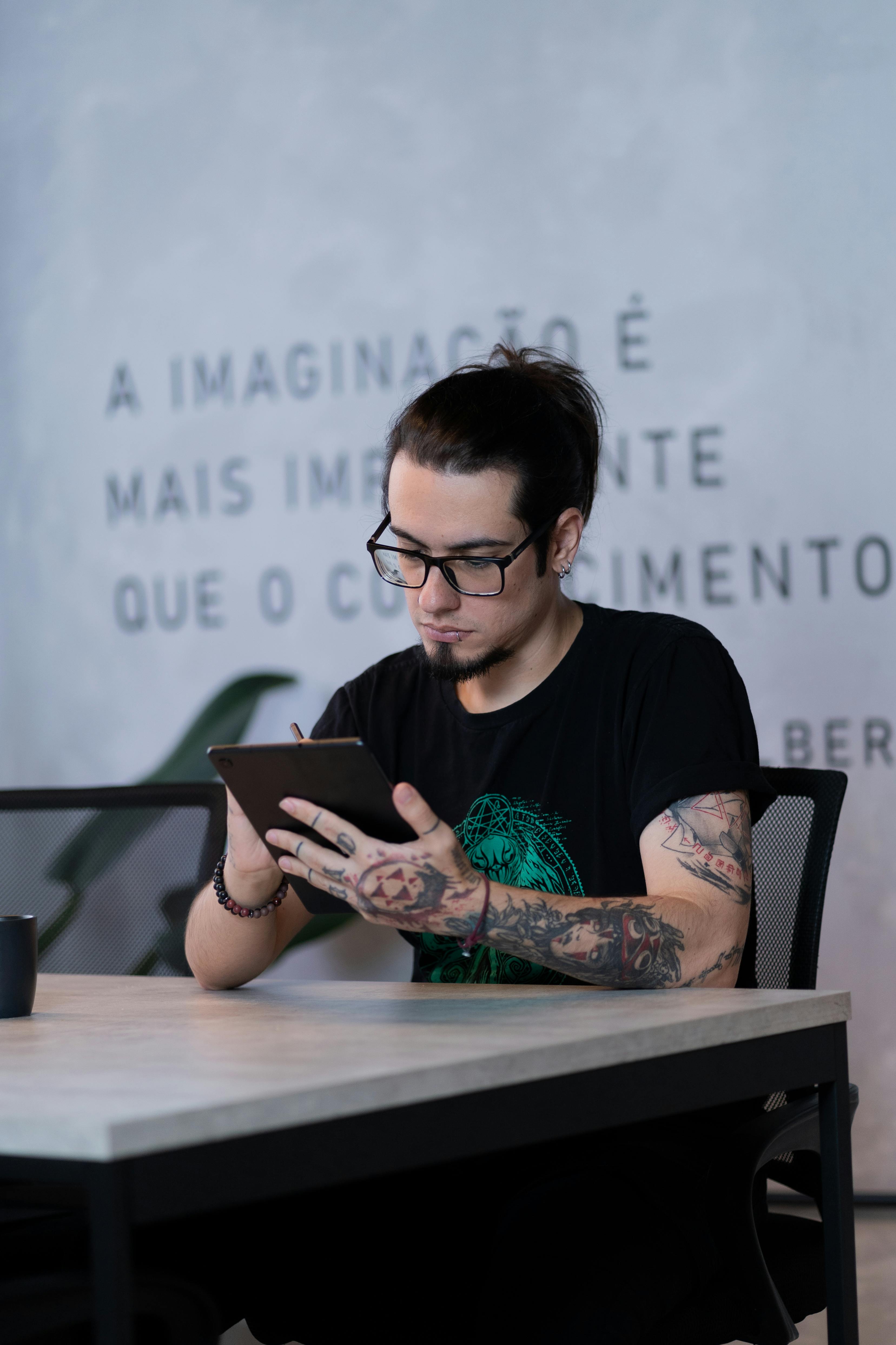 Tattooed adult artist focuses on digital drawing on a tablet indoors.