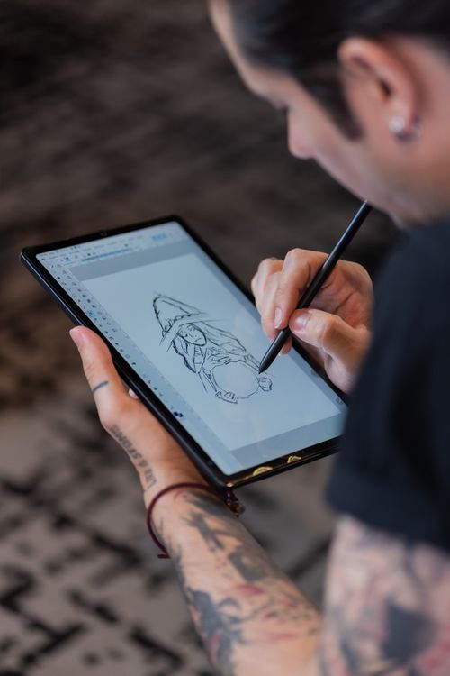 Free A tattooed artist sketching on a tablet using a stylus, focusing on detailed digital artwork. Stock Photo