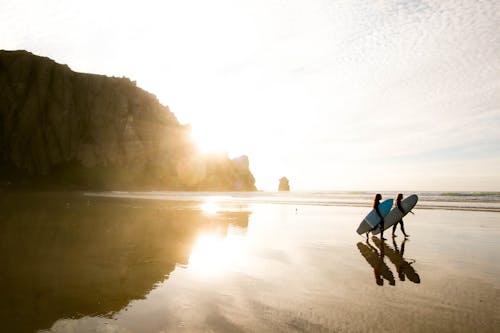 Two People Carrying Surfboards On Seashore