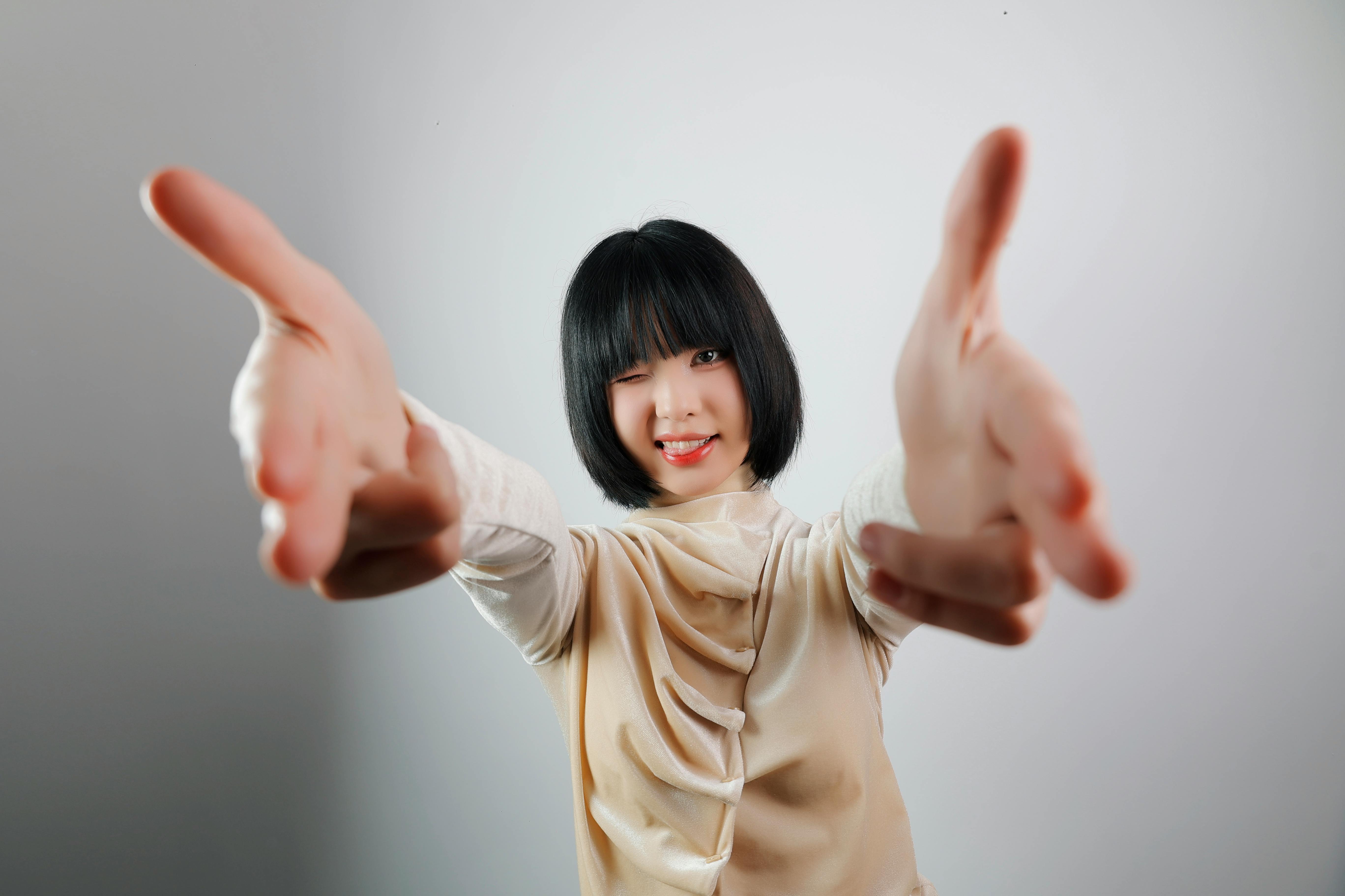 無料 可愛くウインクして両腕を広げた幸せそうな女性が、室内で喜びと遊び心を伝えています。 写真素材