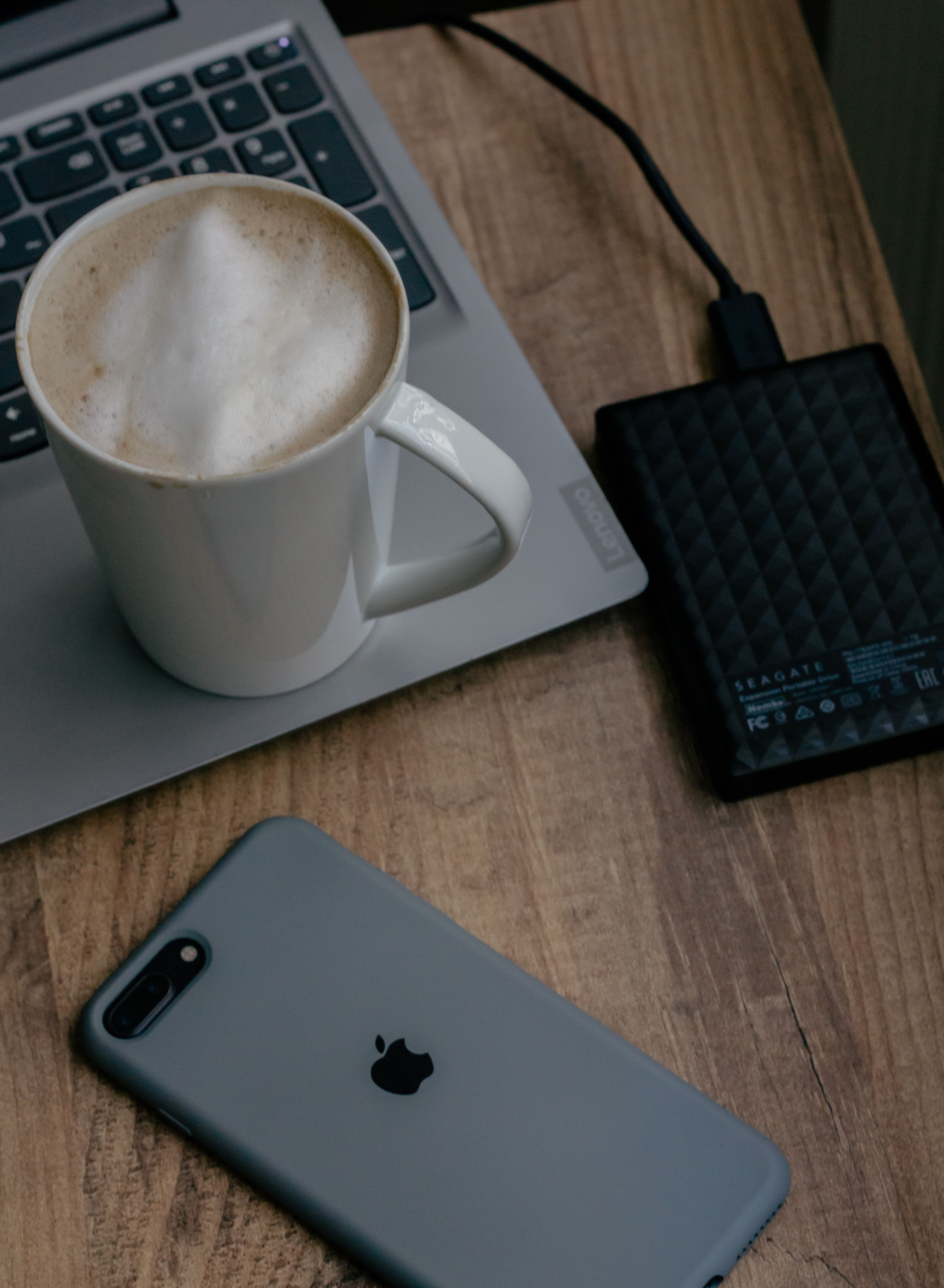 A laptop, phone and coffee cup on a wooden desk