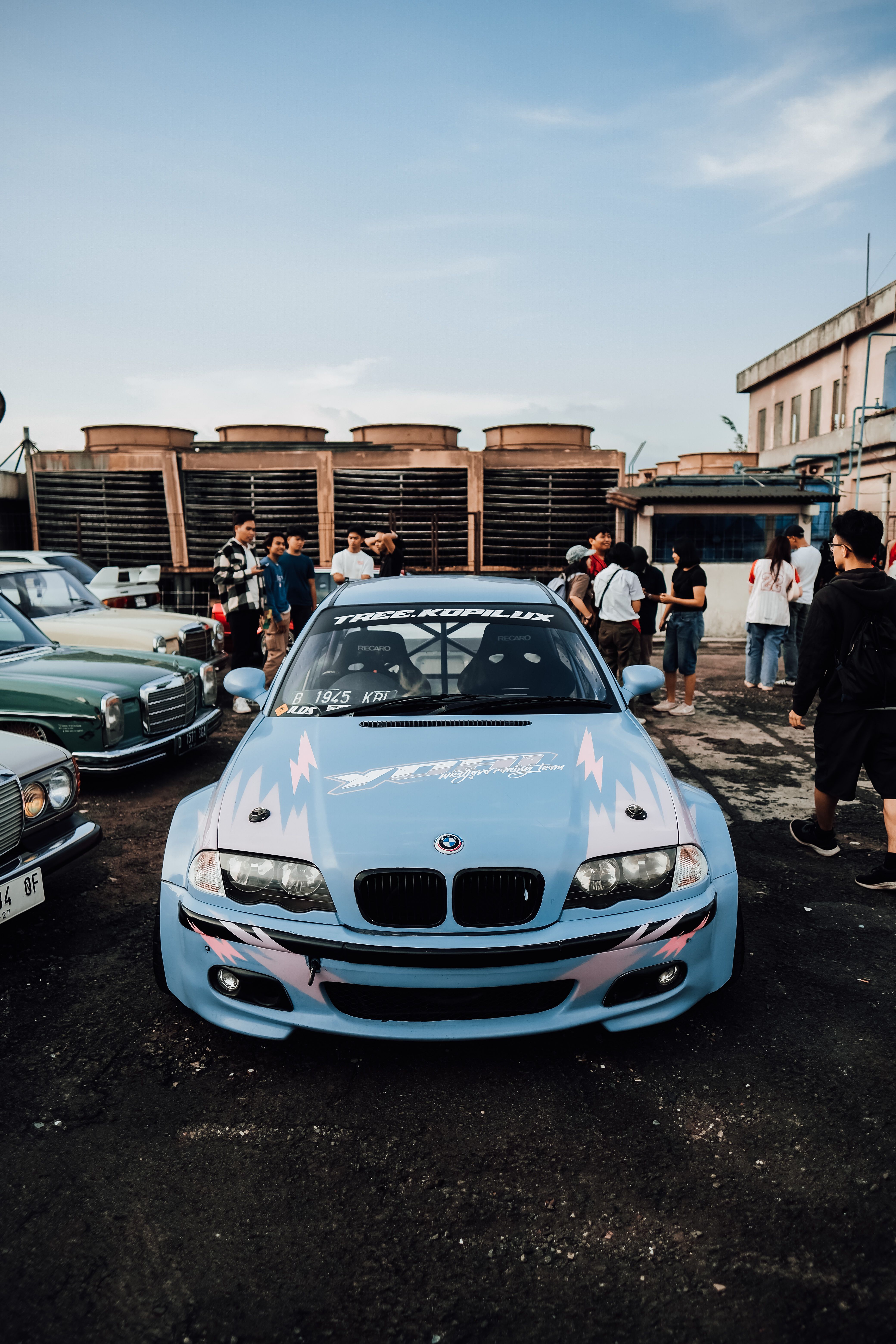 A blue custom car displayed at an outdoor car event with people gathered around.