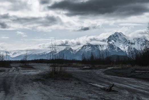 A moody landscape featuring snow-capped mountains under cloudy skies in Alaska.