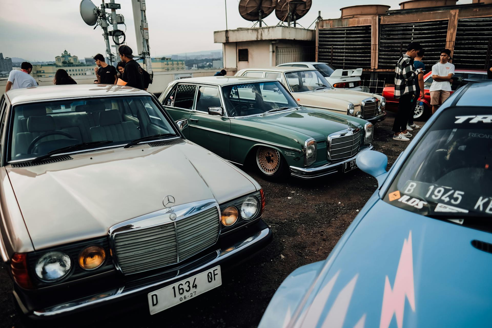 A vintage car meetup on a rooftop with classic vehicles and enthusiasts gathered around.