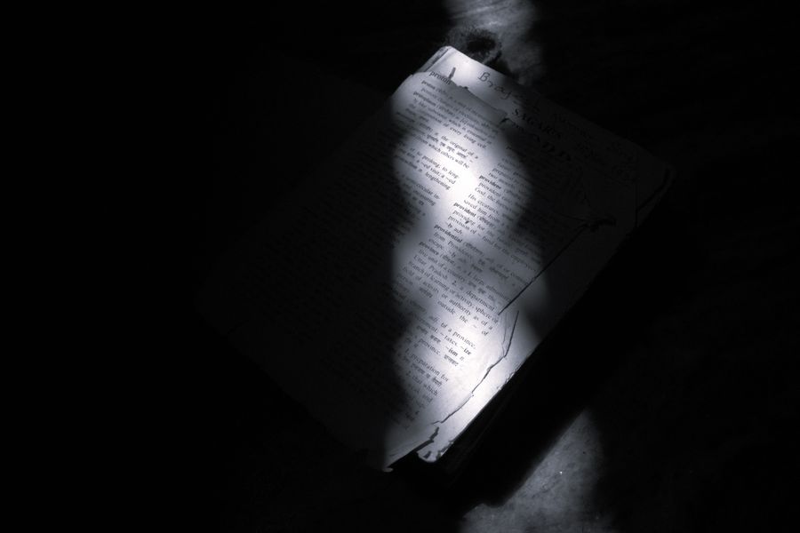 A beam of light casts dramatic shadows on an open book, creating a moody atmosphere.