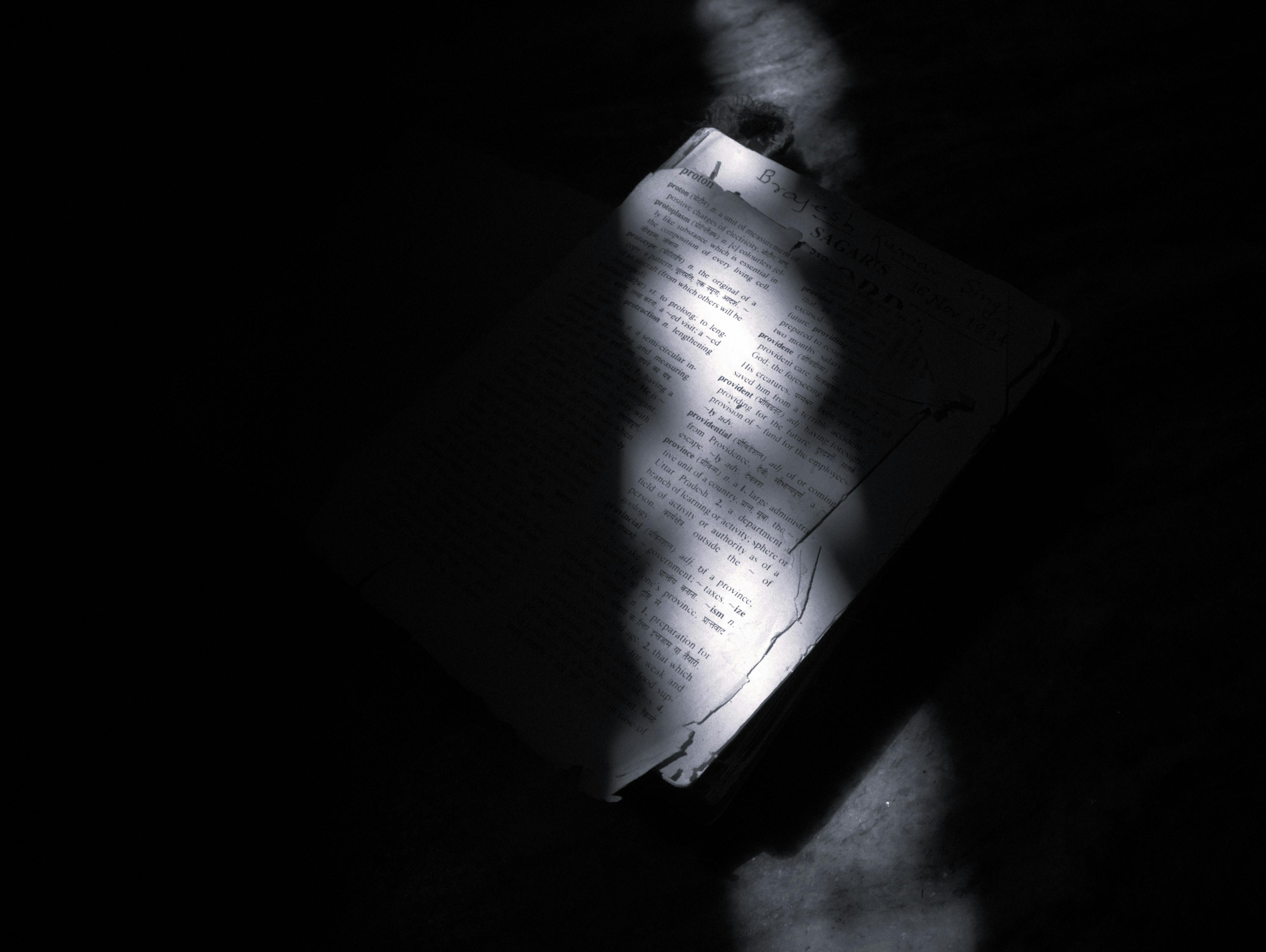 De franc Un feix de llum projecta ombres dramàtiques sobre un llibre obert, creant una atmosfera de mal humor. Foto d'estoc