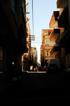 A shadowed urban alley with residential buildings and clear sky.