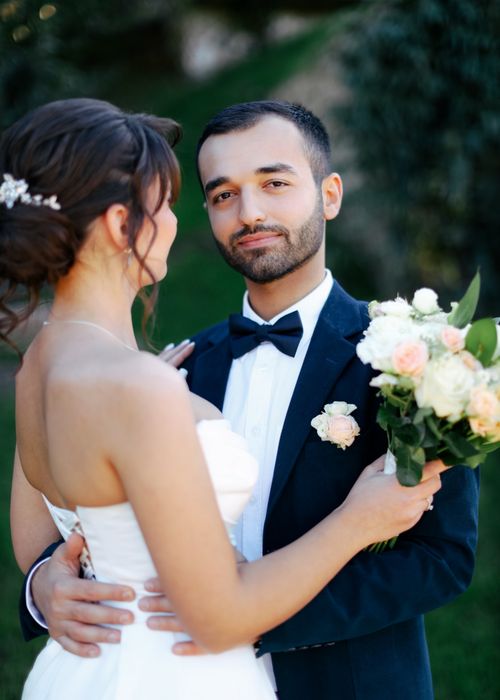 Free A loving couple in wedding attire sharing a moment outdoors with a bouquet. Stock Photo