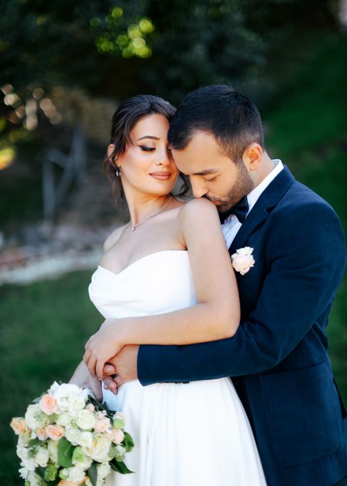 Free A bride and groom share a tender moment outdoors, captured in warm sunlight. Stock Photo