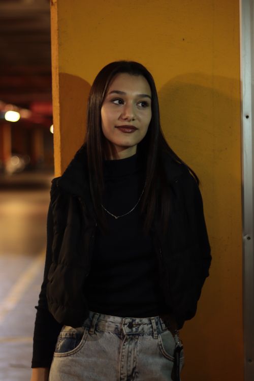 Free Portrait of a young woman leaning against a yellow wall in a dimly lit urban environment. Stock Photo