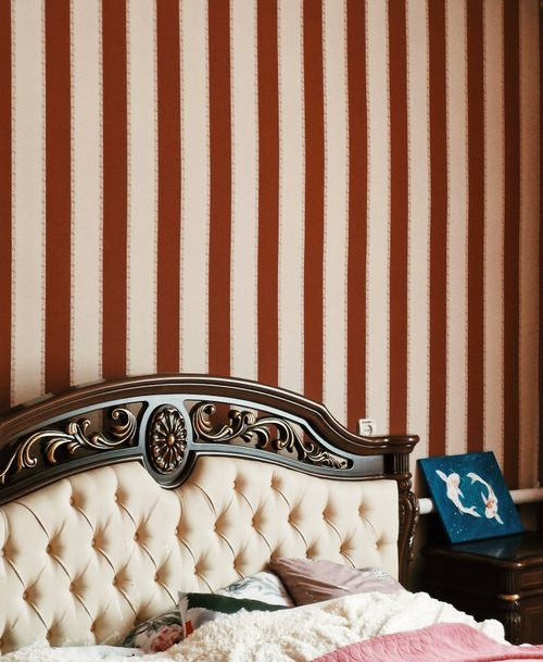 Free Luxurious bedroom featuring a carved wooden headboard and striped wallpaper for a classic look. Stock Photo